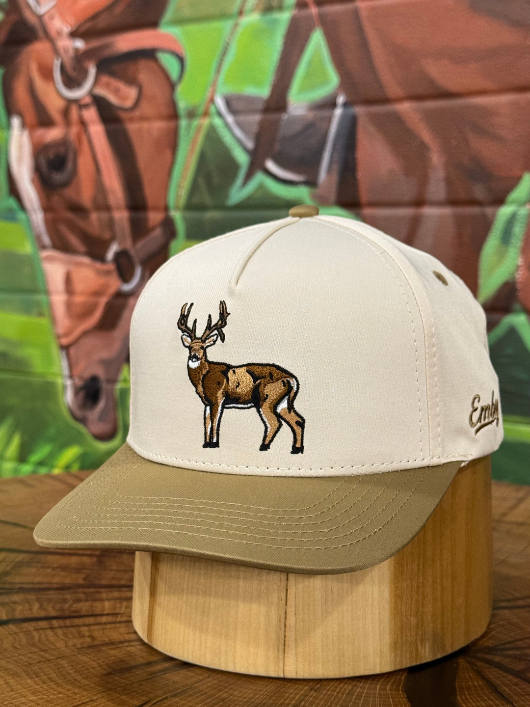 Cap with deer design on a wooden surface with horse mural in the background
